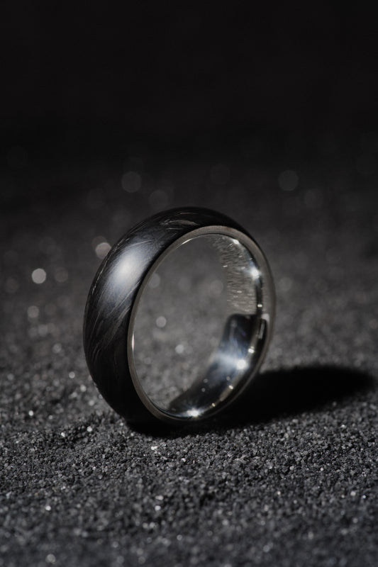 Sterling silver and forged carbon fiber mens wedding band standing on black sand
